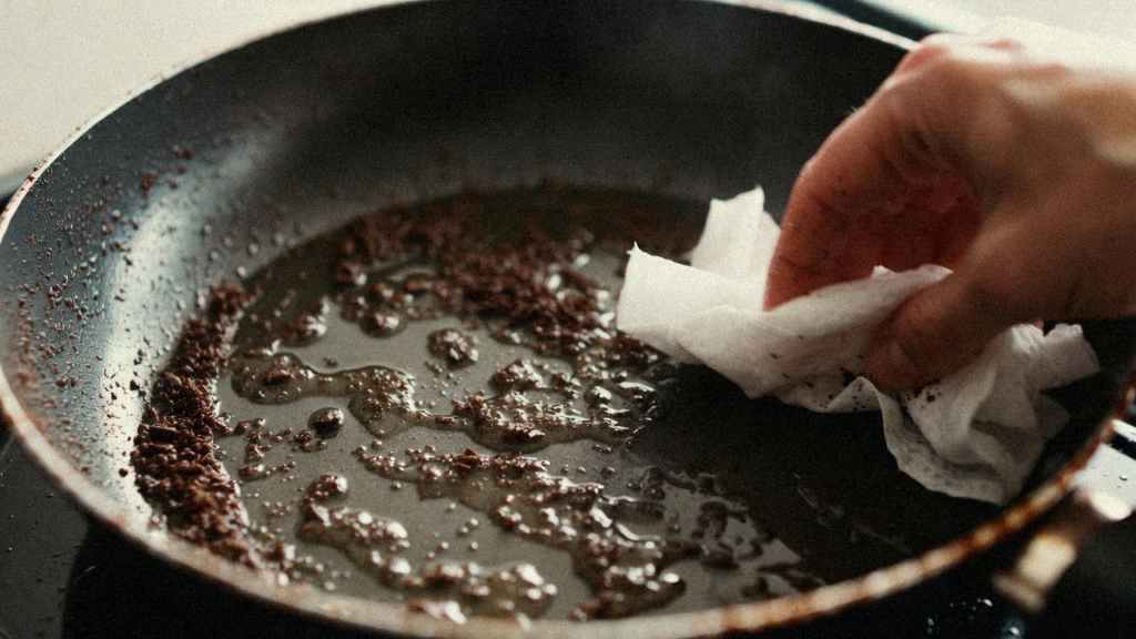 油汚れのついたフライパンにコーヒーかすを振りかけ、油を吸着させている掃除の様子