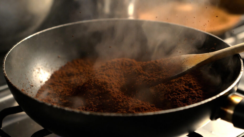フライパンでコーヒーかすを木べらで混ぜながら乾煎りし、水分を飛ばしている様子