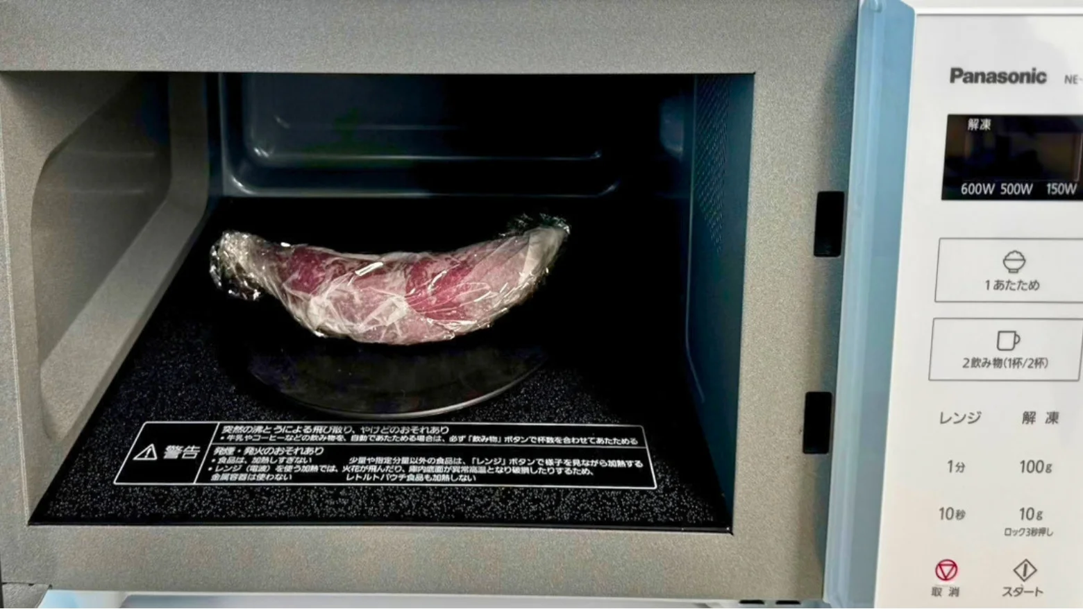 ラップで包んださつまいもを入れた電子レンジ。表示窓に解凍モードが表示されている。