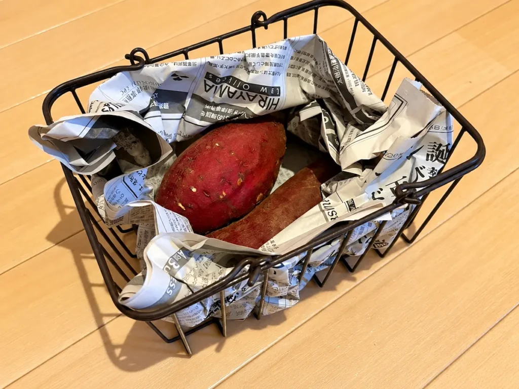 新聞紙で包んださつまいもをワイヤーカゴに入れた写真